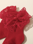 Detaljbild på röd babysocka med spets och rosett vid ankeln