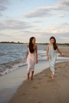 Två flickor går på stranden, en i lila Fiorella maxiklänning och en i ljusblå blommig maxiklänning